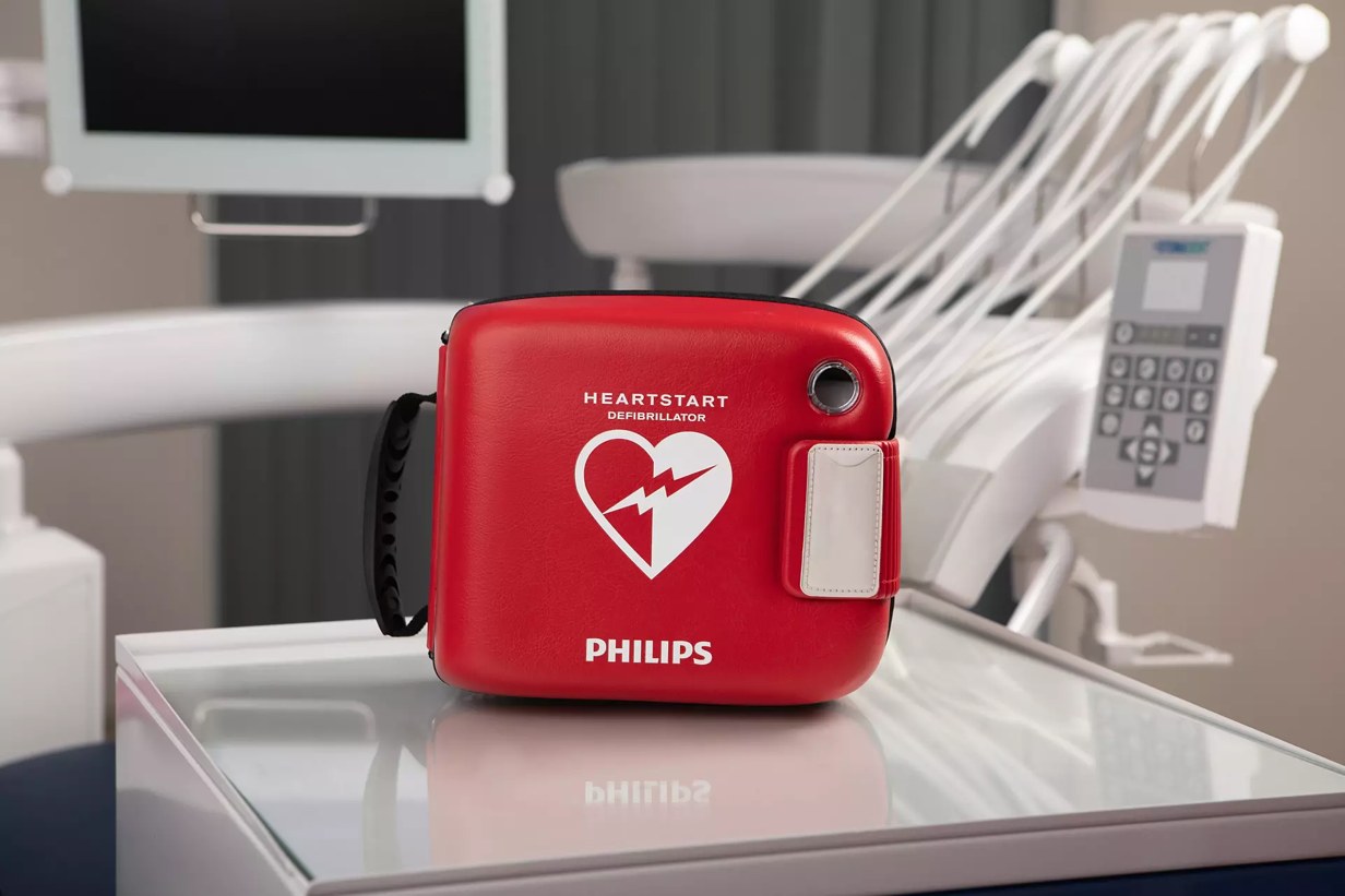 Red Philips HeartStart AED case on a glass-topped cabinet in a clinical room