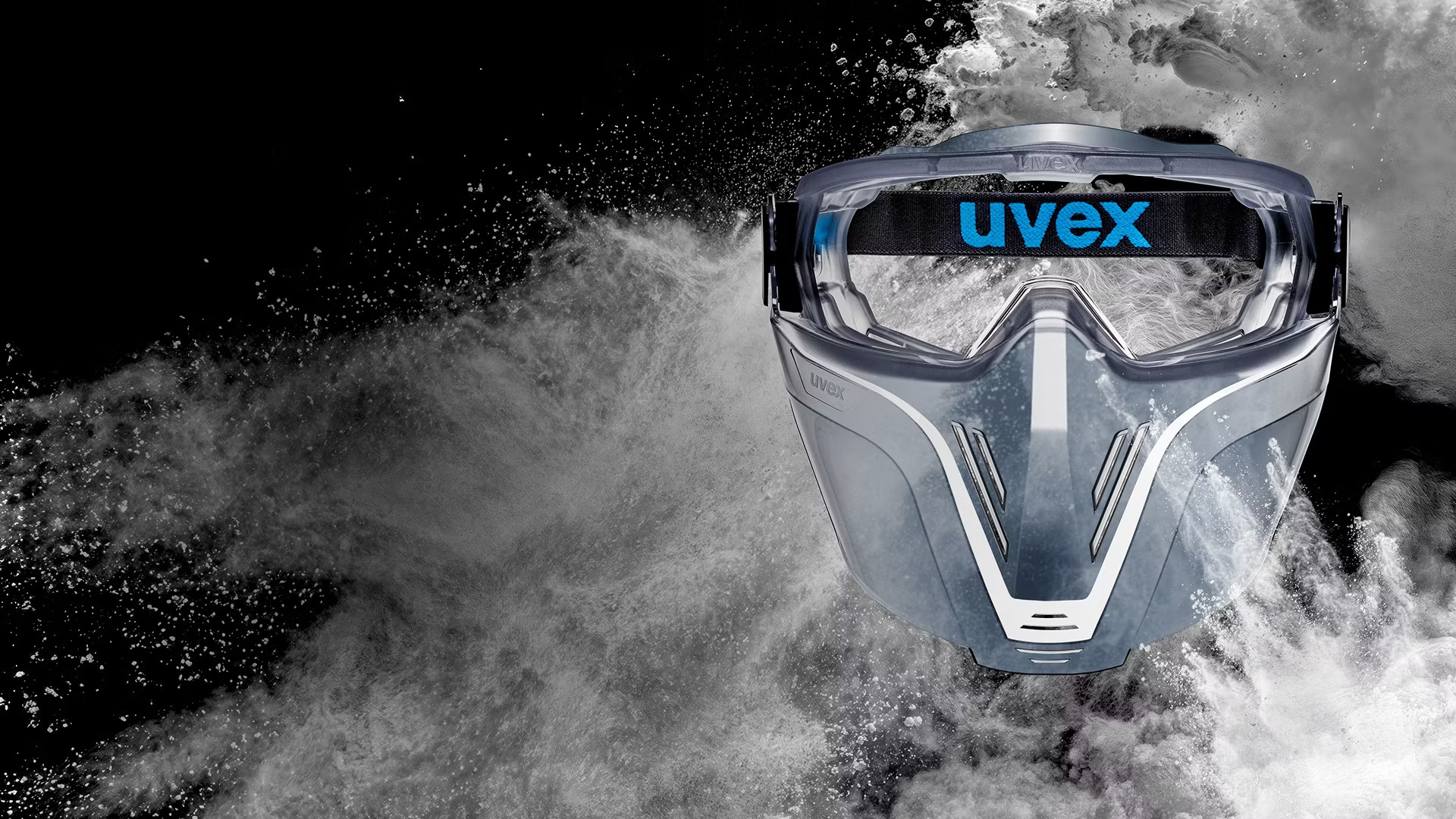Uvex safety goggles fitted with a face guard, shown against a cloud of dust